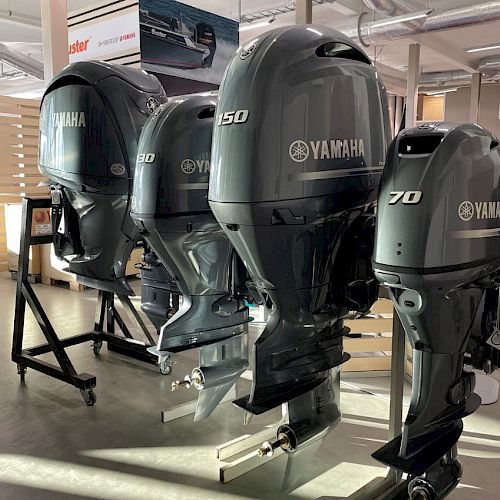 The image shows several Yamaha outboard motors displayed indoors. They are lined up in varying sizes, including models labeled 250, 150, and 70.